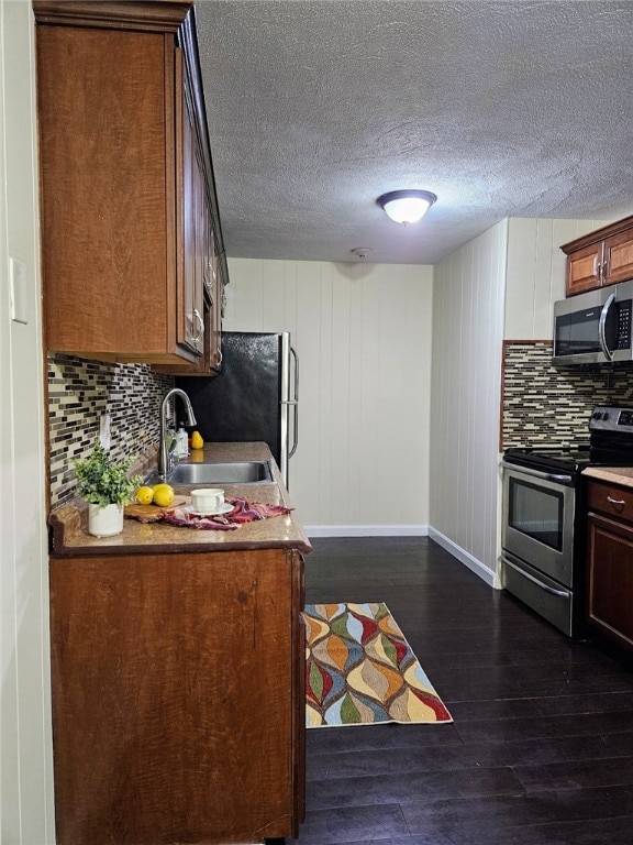 kitchen with sink, wooden walls, decorative backsplash, appliances with stainless steel finishes, and dark hardwood / wood-style flooring