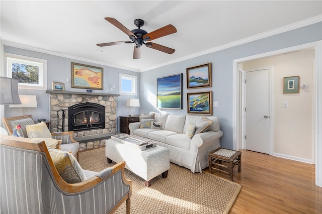 living room featuring a stone fireplace, light wood-type flooring, ornamental molding, and plenty of natural light