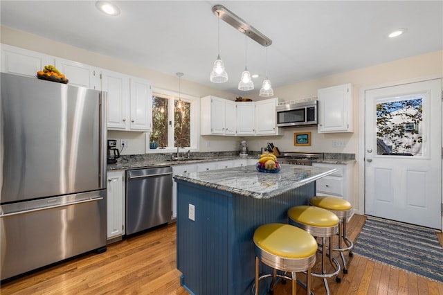 kitchen featuring light stone counters, stainless steel appliances, a kitchen island, white cabinetry, and light hardwood / wood-style flooring