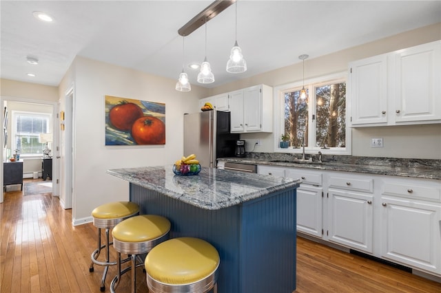 kitchen featuring appliances with stainless steel finishes, a kitchen bar, a kitchen island, white cabinets, and light wood-type flooring