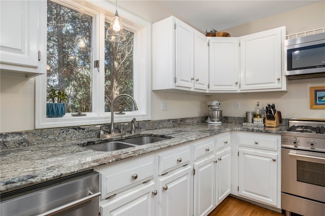 kitchen with stainless steel appliances, white cabinetry, light stone countertops, sink, and light hardwood / wood-style flooring