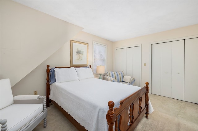 bedroom with multiple closets, light carpet, and vaulted ceiling