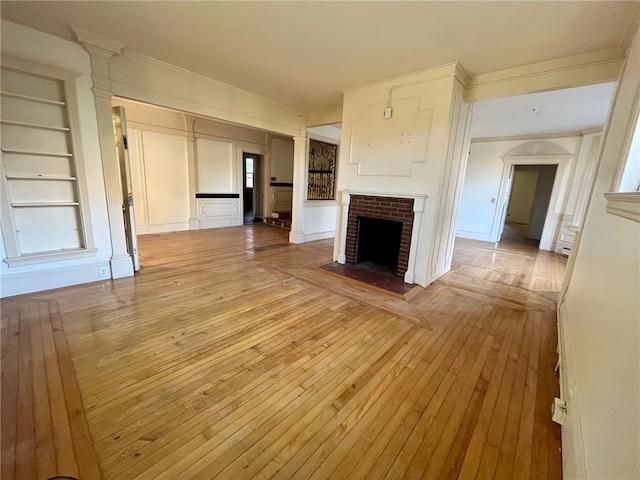 unfurnished living room featuring a fireplace, built in features, light hardwood / wood-style flooring, and crown molding