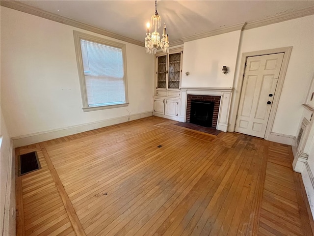 unfurnished living room featuring a brick fireplace, hardwood / wood-style floors, ornamental molding, and an inviting chandelier