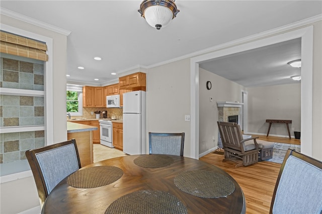 dining room with a tile fireplace, sink, light wood-type flooring, and ornamental molding