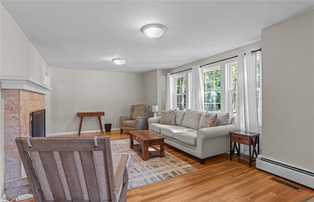 living room featuring a baseboard radiator, a tile fireplace, and light hardwood / wood-style flooring