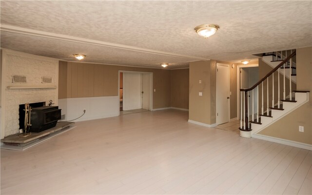 unfurnished living room with a textured ceiling, a wood stove, and light hardwood / wood-style flooring