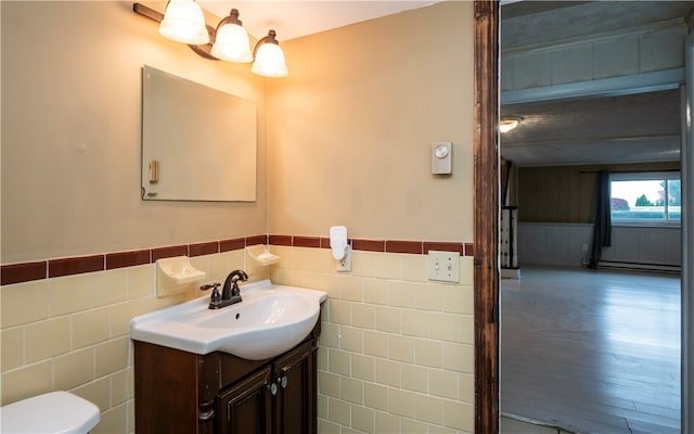 bathroom featuring hardwood / wood-style flooring, vanity, a baseboard radiator, toilet, and tile walls