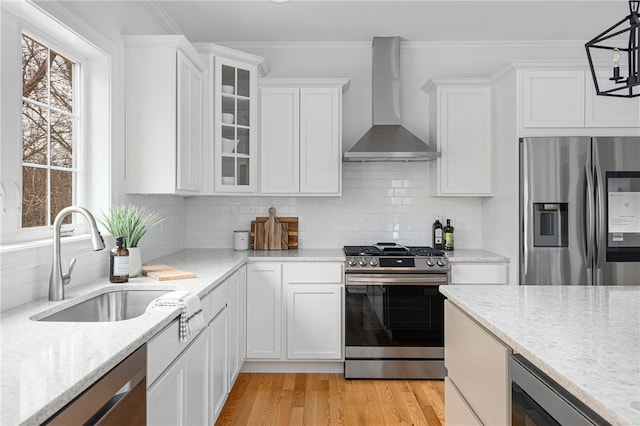 kitchen featuring stainless steel appliances, white cabinetry, sink, wall chimney exhaust hood, and pendant lighting