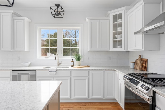 kitchen with stainless steel appliances, white cabinetry, wall chimney range hood, sink, and light hardwood / wood-style flooring