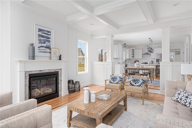 living room with beam ceiling, coffered ceiling, crown molding, decorative columns, and light wood-type flooring