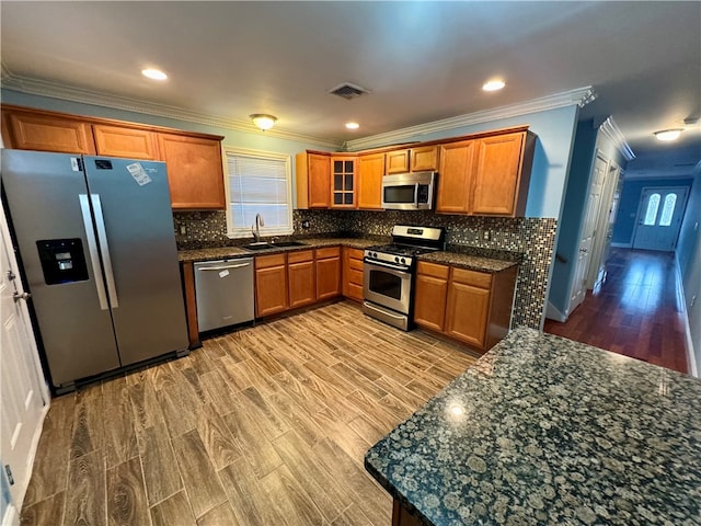 kitchen with light wood-type flooring, dark stone counters, stainless steel appliances, crown molding, and sink