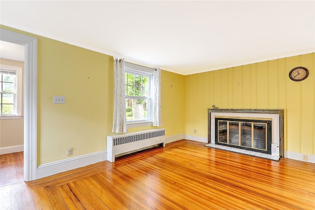 unfurnished living room with wooden walls, radiator heating unit, hardwood / wood-style floors, and crown molding