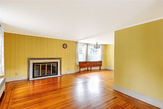 unfurnished living room featuring wood-type flooring, wooden walls, an inviting chandelier, and crown molding