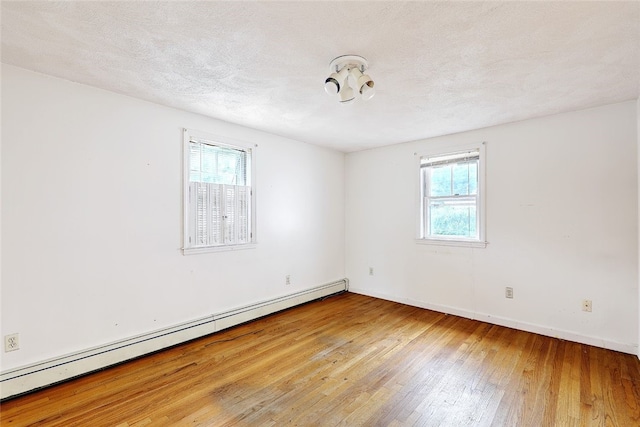 spare room featuring a textured ceiling, hardwood / wood-style floors, a healthy amount of sunlight, and a baseboard heating unit