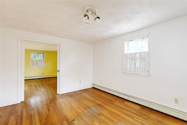 unfurnished room with a baseboard heating unit, plenty of natural light, and light hardwood / wood-style flooring