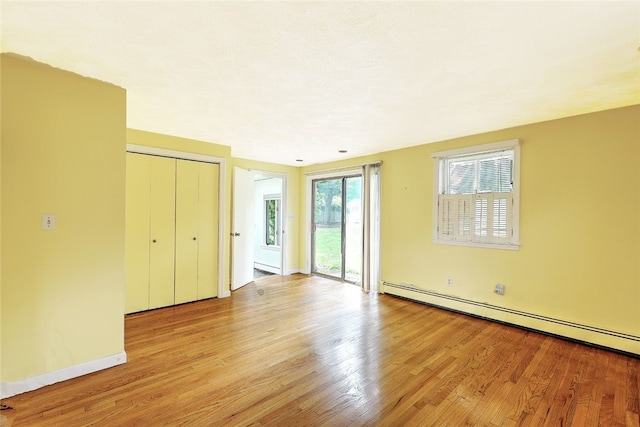 unfurnished bedroom with access to exterior, a closet, light hardwood / wood-style flooring, and a baseboard heating unit