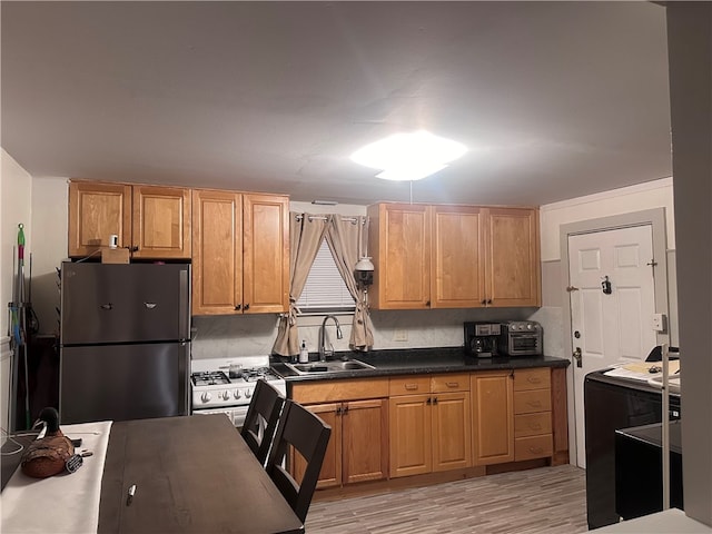 kitchen with white gas stove, sink, tasteful backsplash, stainless steel fridge, and light wood-type flooring