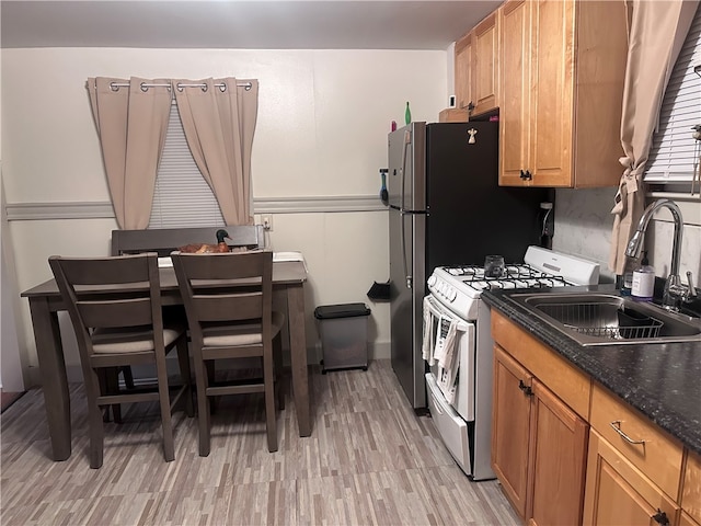 kitchen featuring dark stone counters, light wood-type flooring, white range with gas cooktop, and sink