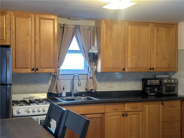 kitchen with stainless steel fridge, sink, white gas range oven, and tasteful backsplash