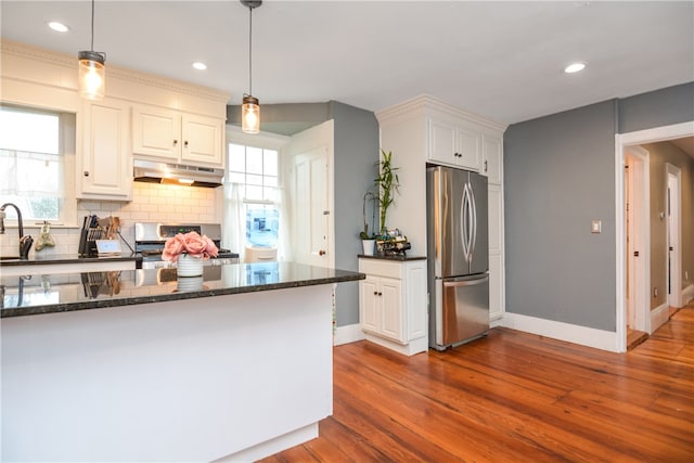 kitchen featuring light hardwood / wood-style floors, white cabinetry, appliances with stainless steel finishes, dark stone countertops, and pendant lighting