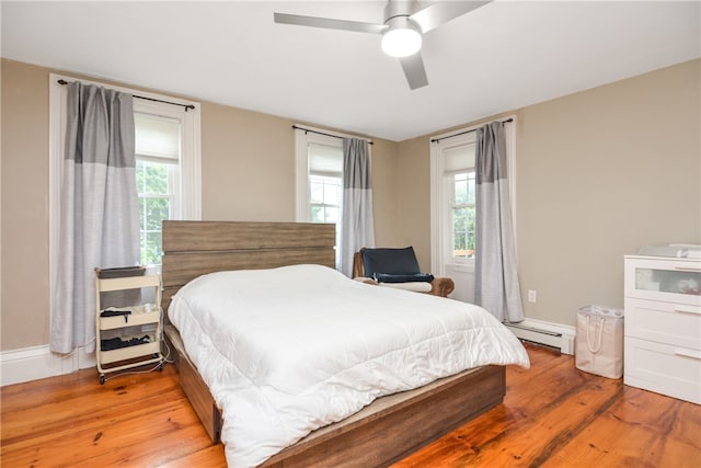 bedroom featuring a baseboard heating unit, multiple windows, ceiling fan, and light hardwood / wood-style flooring