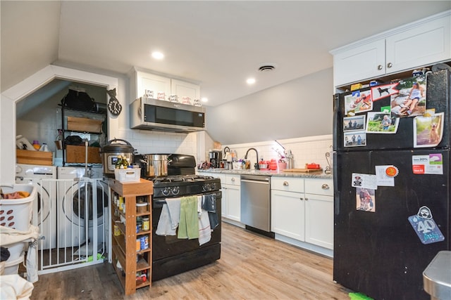 kitchen with white cabinets, black appliances, washer and clothes dryer, and light hardwood / wood-style flooring