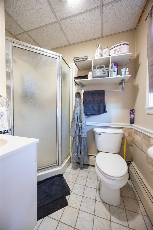 bathroom with a baseboard heating unit, a drop ceiling, tile patterned flooring, vanity, and a shower with shower door