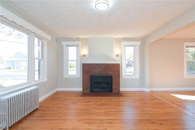 unfurnished living room with radiator heating unit, light hardwood / wood-style floors, and a brick fireplace