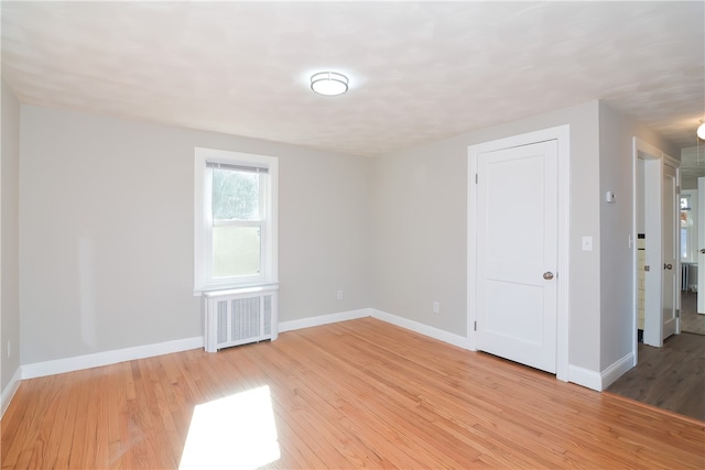 spare room featuring radiator heating unit and light hardwood / wood-style floors