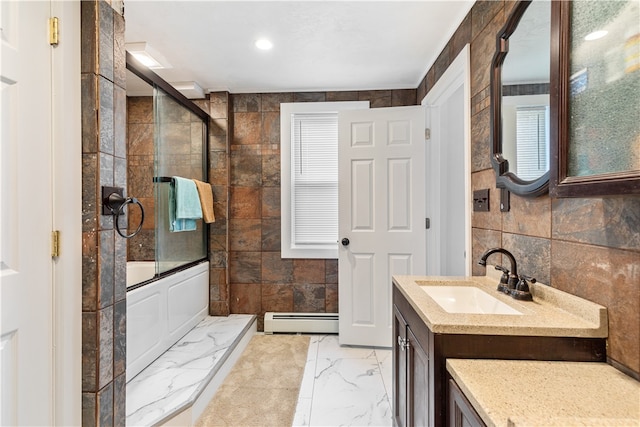 bathroom with baseboard heating, bath / shower combo with glass door, tile walls, and vanity