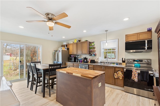 kitchen featuring appliances with stainless steel finishes, pendant lighting, light stone countertops, sink, and light hardwood / wood-style flooring