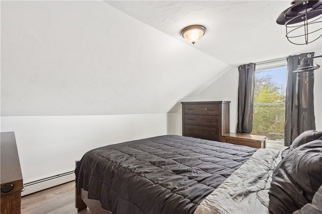 bedroom with baseboard heating, light wood-type flooring, and vaulted ceiling