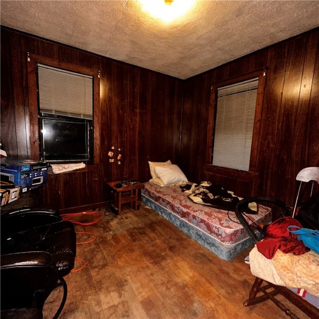 bedroom featuring hardwood / wood-style floors, wooden walls, and a textured ceiling