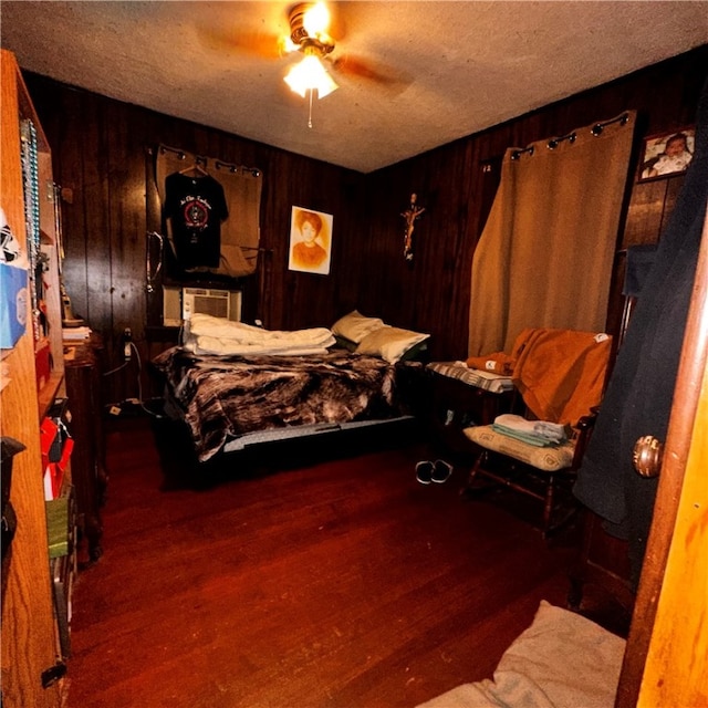 bedroom with a textured ceiling, wooden walls, ceiling fan, and dark hardwood / wood-style floors