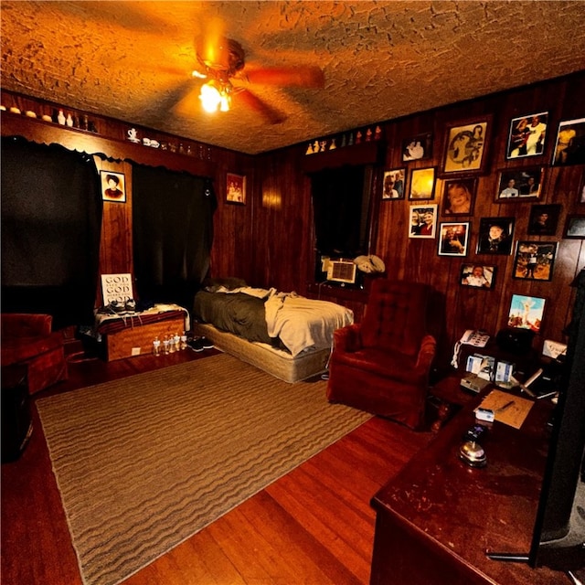 home theater room with wood walls, wood-type flooring, ceiling fan, and a textured ceiling