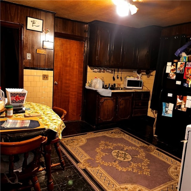 kitchen with dark brown cabinets, tasteful backsplash, and black refrigerator