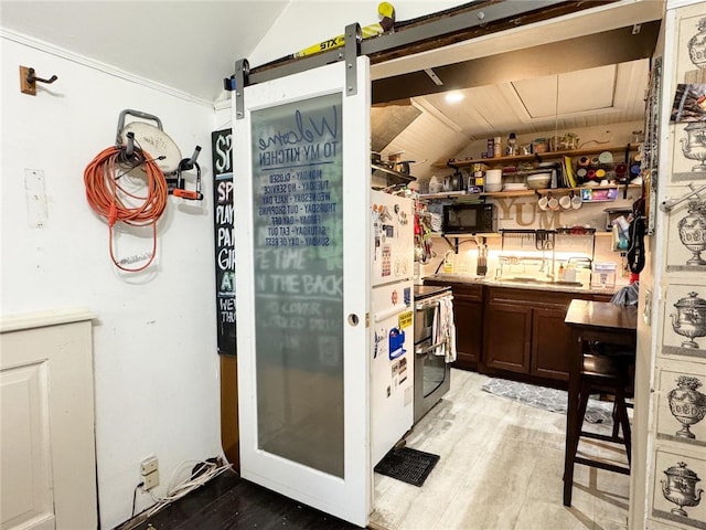 kitchen featuring stainless steel electric range, a barn door, sink, vaulted ceiling, and light hardwood / wood-style flooring