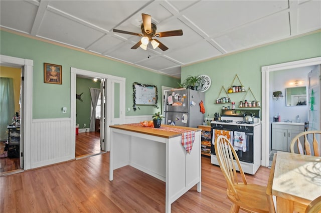 kitchen with stainless steel refrigerator, white gas range, light hardwood / wood-style floors, ceiling fan, and a center island