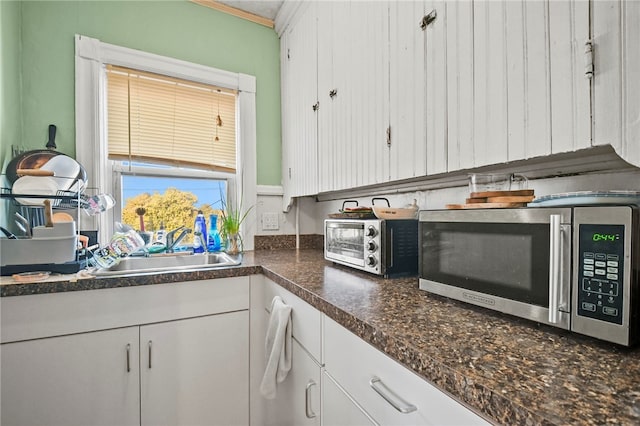 kitchen with white cabinetry, ornamental molding, and sink