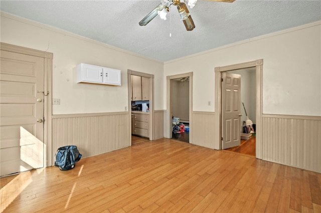 interior space featuring ceiling fan, a textured ceiling, ornamental molding, and light hardwood / wood-style flooring