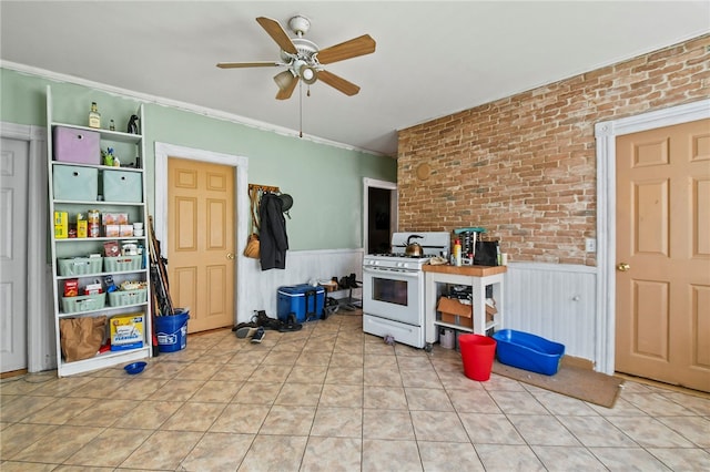 kitchen featuring gas range gas stove, brick wall, ornamental molding, ceiling fan, and light tile patterned floors