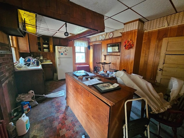 kitchen with dark colored carpet, wooden walls, white refrigerator, and radiator