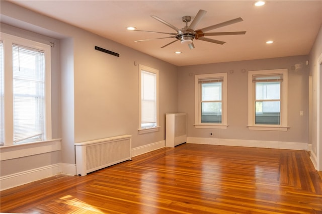 empty room featuring a wealth of natural light, radiator heating unit, hardwood / wood-style floors, and ceiling fan