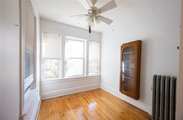 unfurnished room with ceiling fan, radiator heating unit, light hardwood / wood-style floors, and plenty of natural light