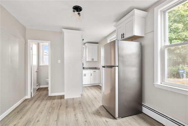 kitchen featuring a wealth of natural light, stainless steel refrigerator, white cabinetry, and baseboard heating