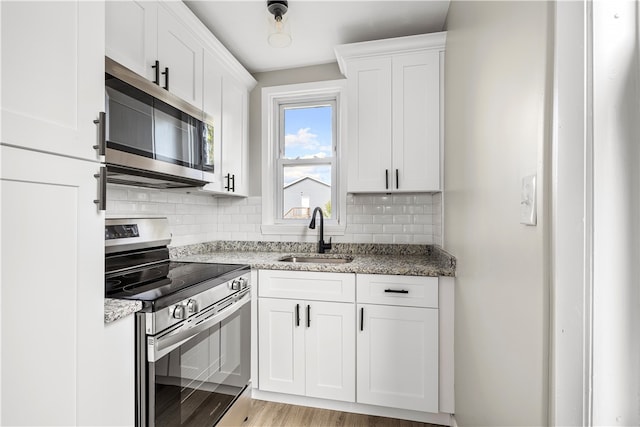 kitchen with white cabinets, stainless steel appliances, sink, and light stone counters