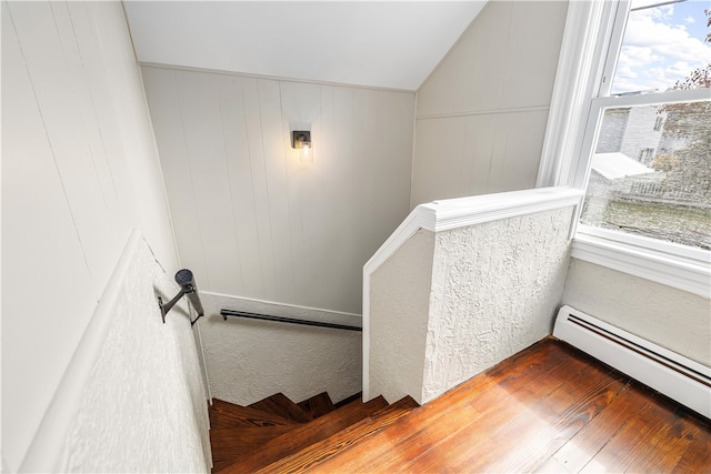 stairs featuring wooden walls, lofted ceiling, wood-type flooring, and a baseboard heating unit