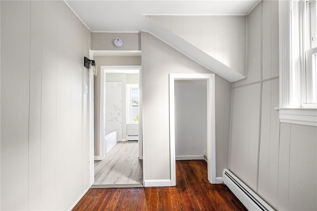 hallway featuring a baseboard heating unit, wood walls, and dark hardwood / wood-style floors