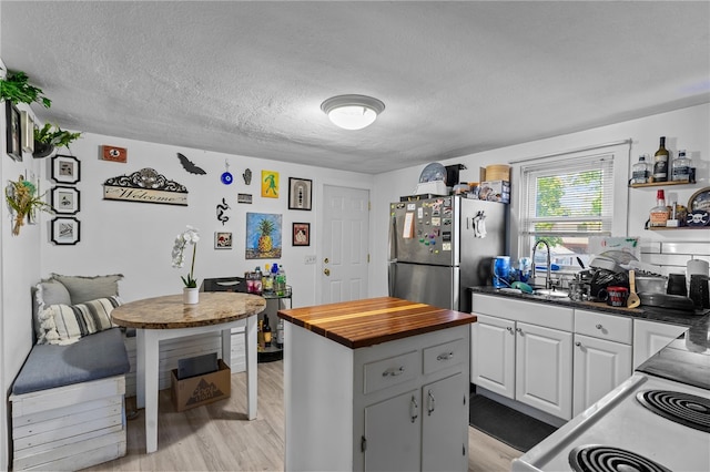 kitchen with white cabinets, sink, stainless steel fridge, light wood-type flooring, and a textured ceiling